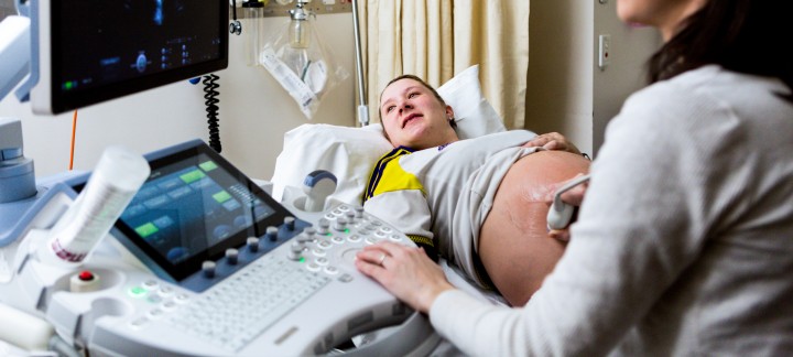 A pregnant woman and an ultrasound technician smile at the screen during an ultrasound.